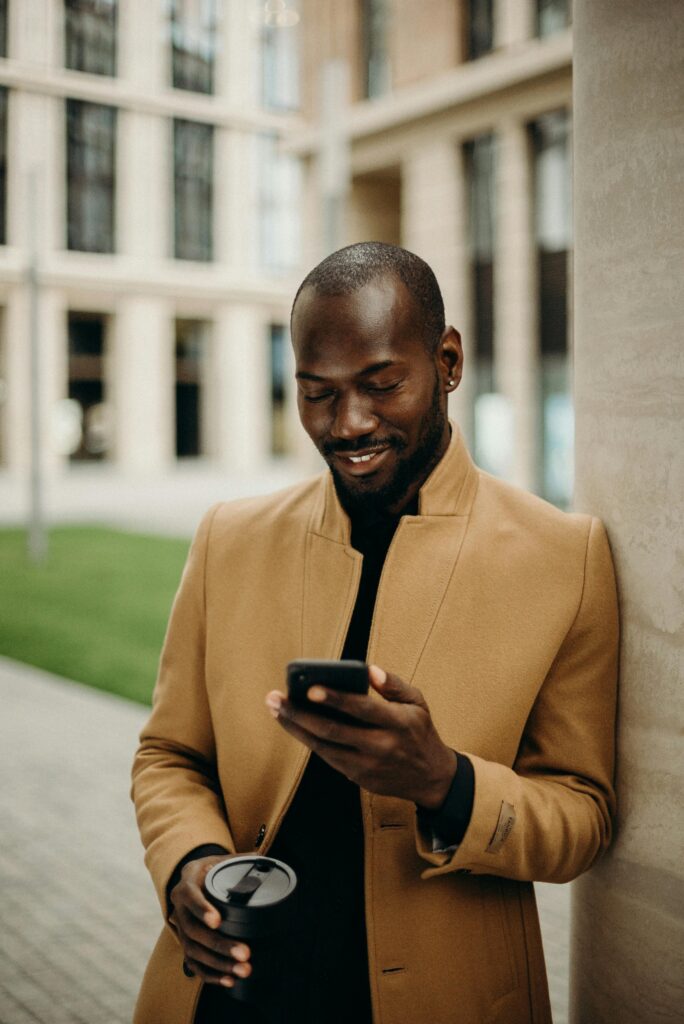 Selective Focus Photo of Smiling Man Looking at His Phone While Holding Cup